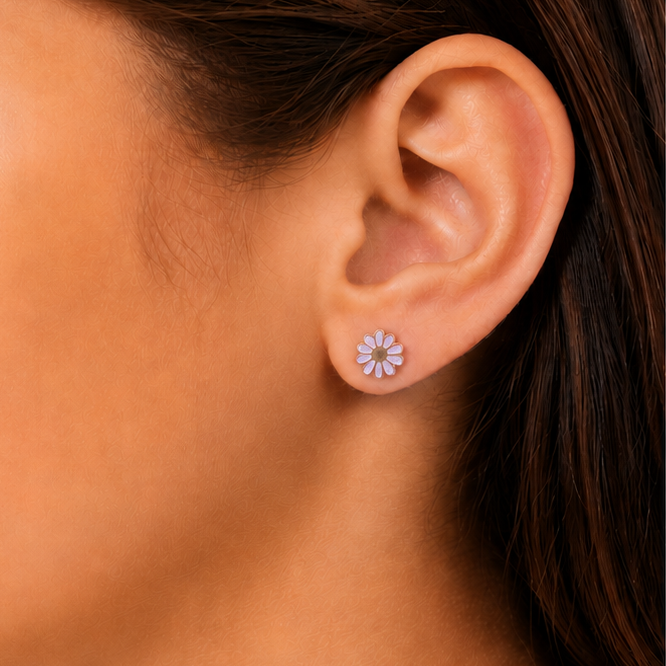 Close up of a girl wearing floral earrings with a matching brooch on a light gray background.