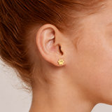 Close-up of a person wearing gold paw print earrings with a neutral background