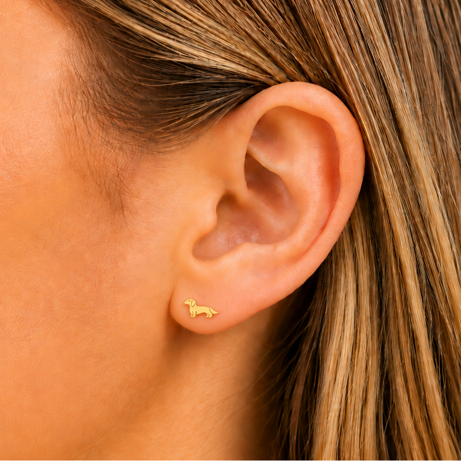 Close-up of a person wearing a gold dachsund earring with a plain background