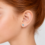 Close-up of a person wearing a small blue lightning bolt earring on a plain background