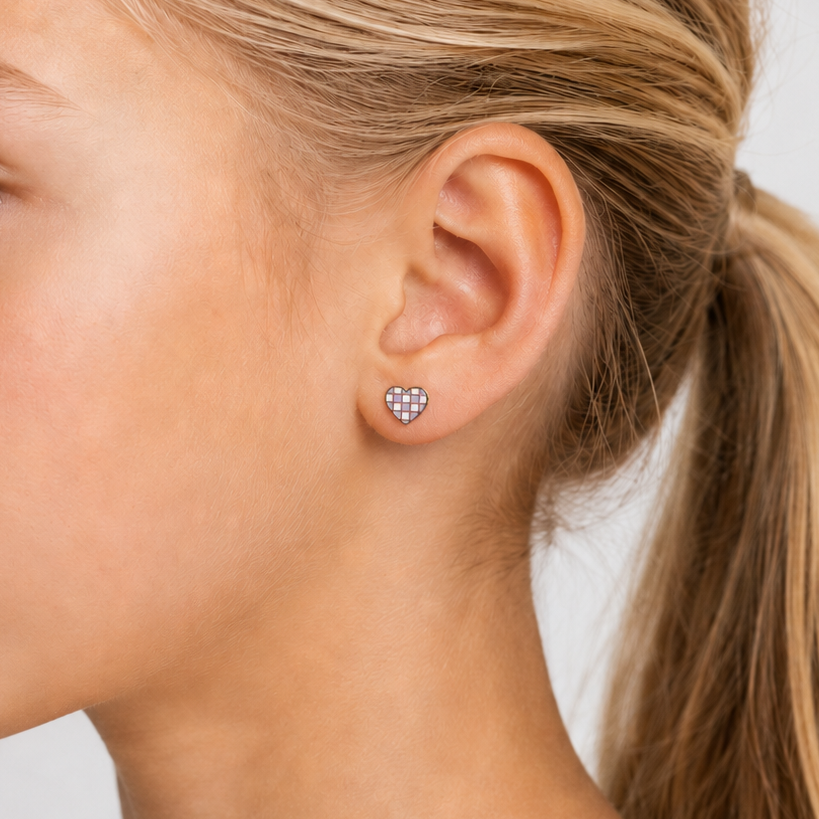 Close-up of a young girl wearing stud heart earring checkered white and purple  with a plain background